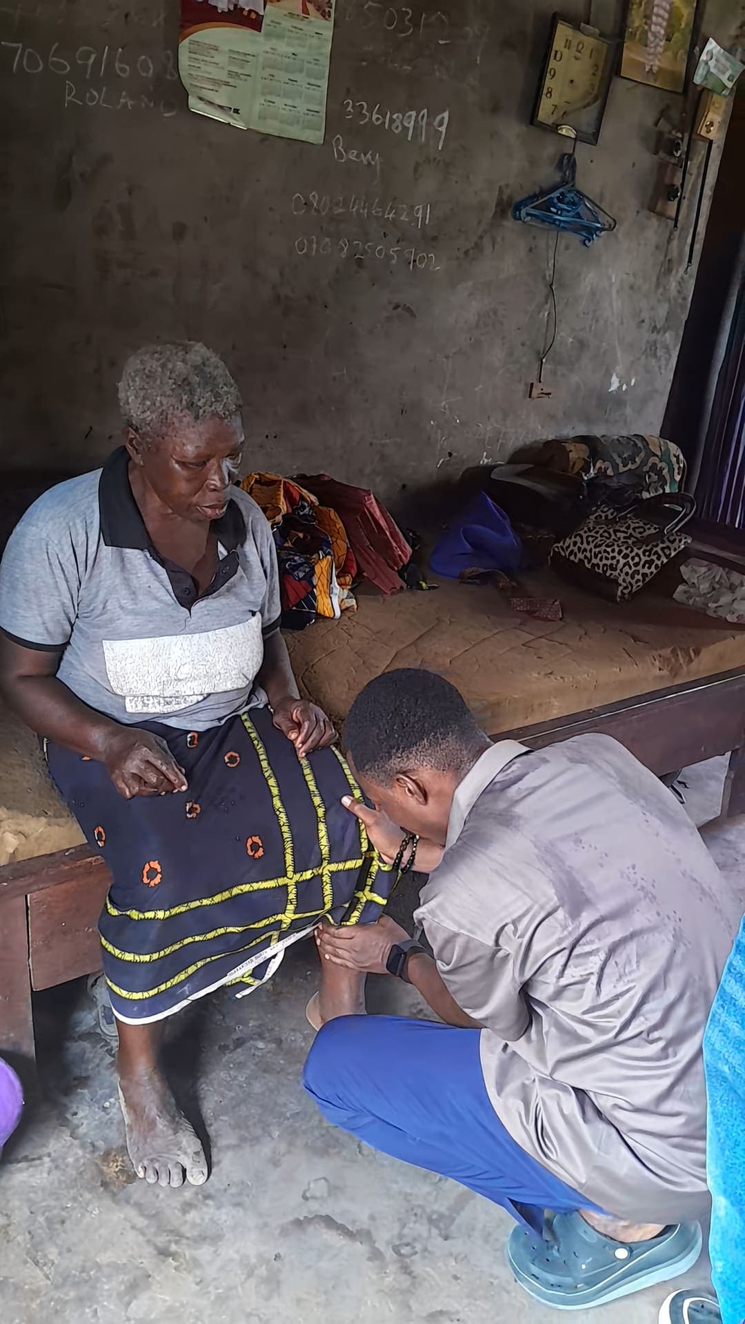 A volunteer kneels beside an elderly woman in her home during the Eku outreach, December 2025